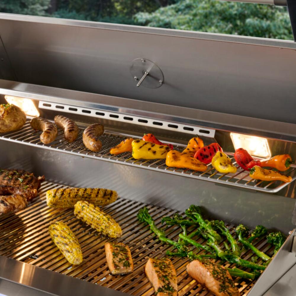 Open stainless gas grill with food on grates and long burner bar beneath the hood