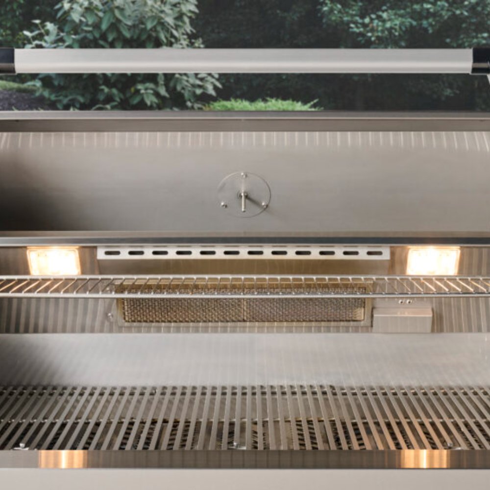 Open built-in gas grill interior with warming rack above grates and food on burners