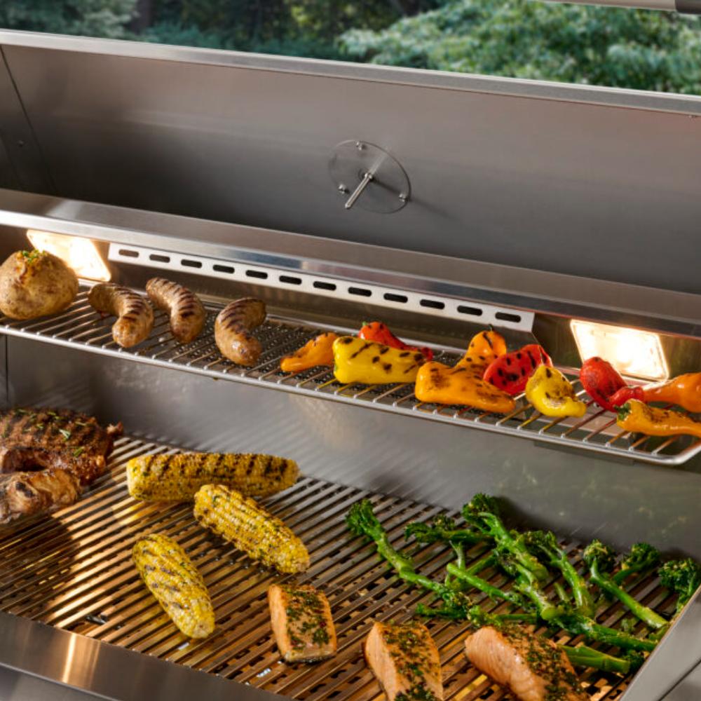 Open built-in gas grill showing warming rack, seared vegetables and meats on grates