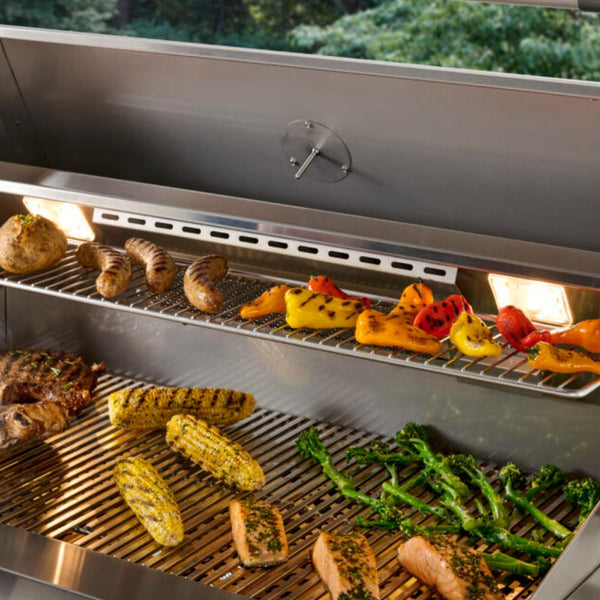 Open built-in gas grill showing warming rack, seared vegetables and meats on grates