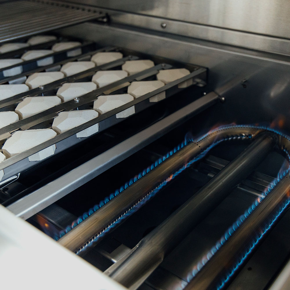 Gas grill burner tubes and cooking grates with blue flames under the grate