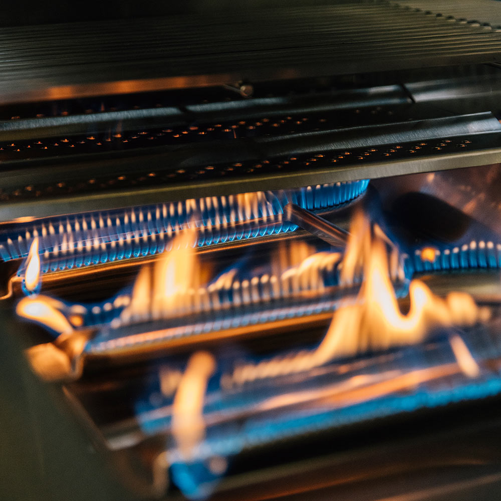 Gas grill interior with glowing burners and orange flames across the firebox