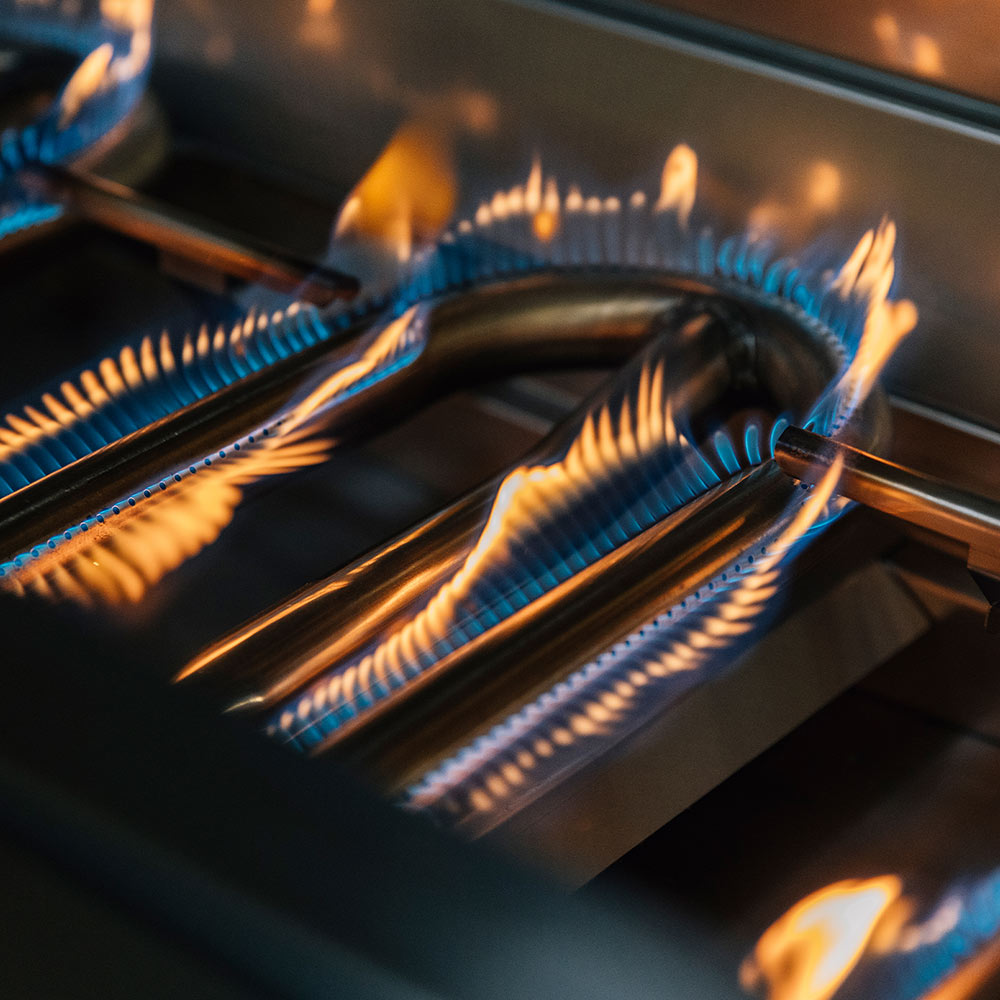 Gas grill burners with blue flames and orange fire, close-up inside the grill