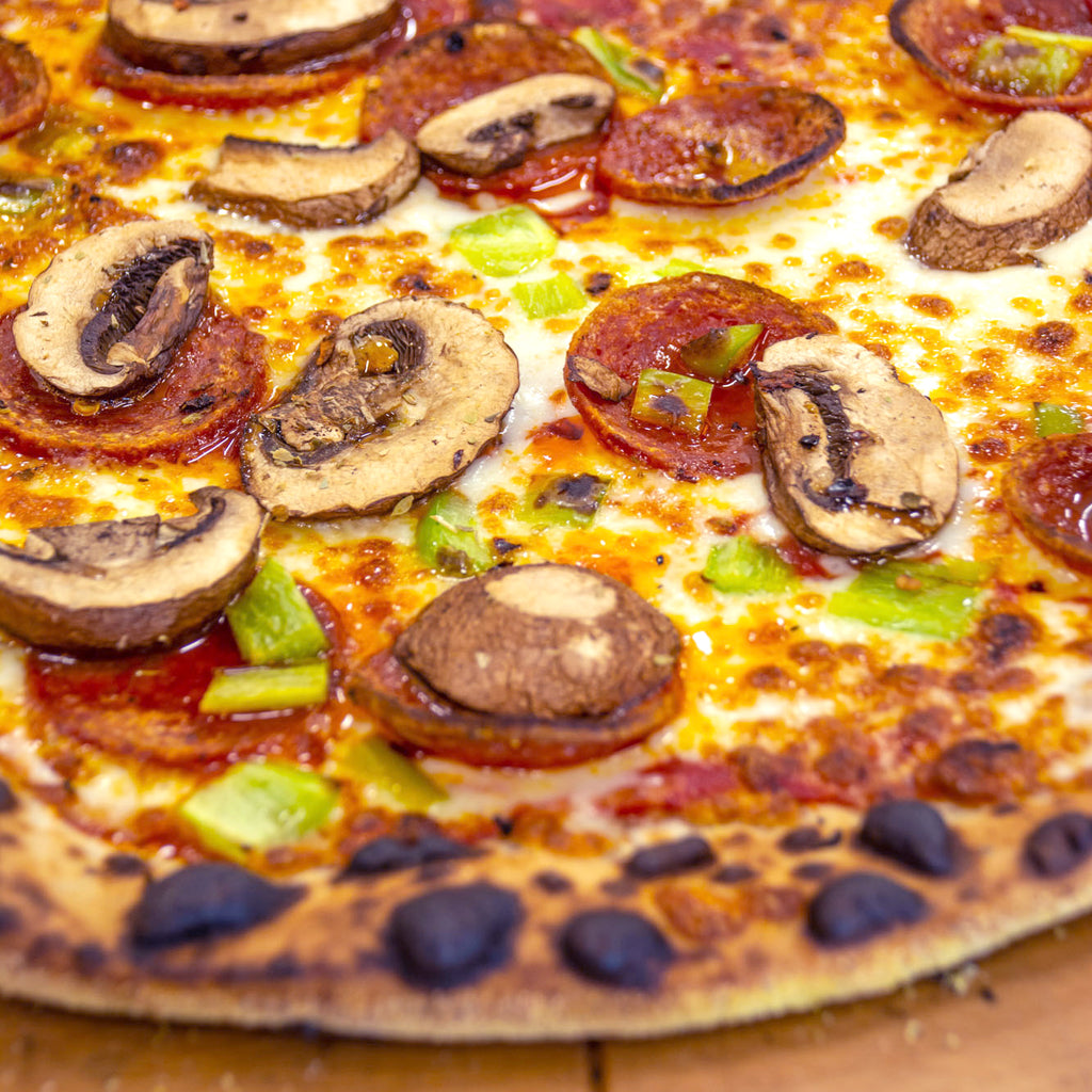 Fresh pizza with mushrooms, pepperoni, and vegetables on a wood-fired crust