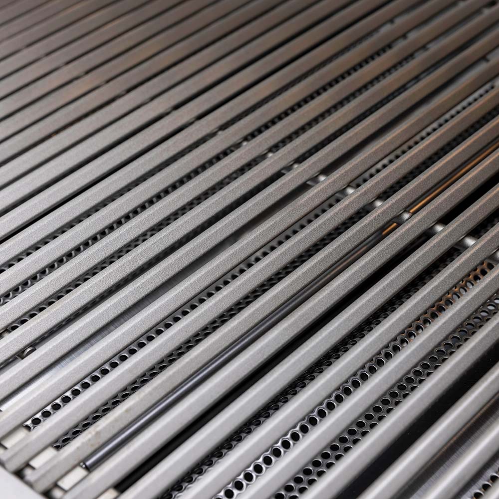 Outdoor grill burner area with stainless grates and rows of igniter holes