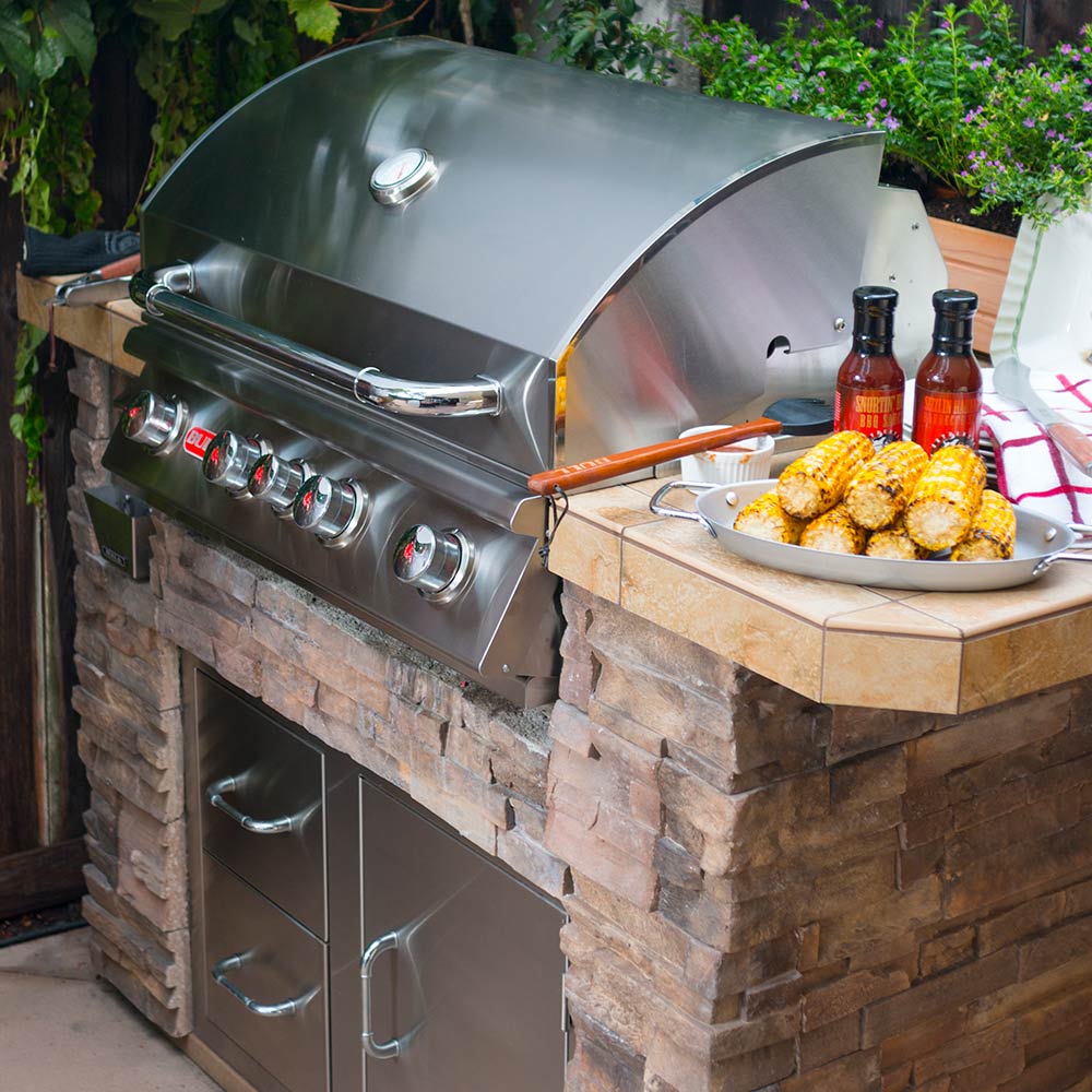 Outdoor built-in gas grill with closed lid, burner knobs, and side serving counter