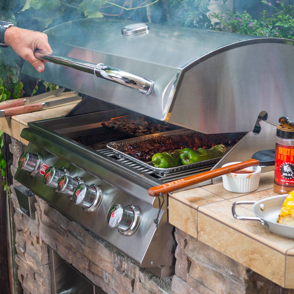 Stainless steel built-in gas grill with open hood, cooking grates, and food inside