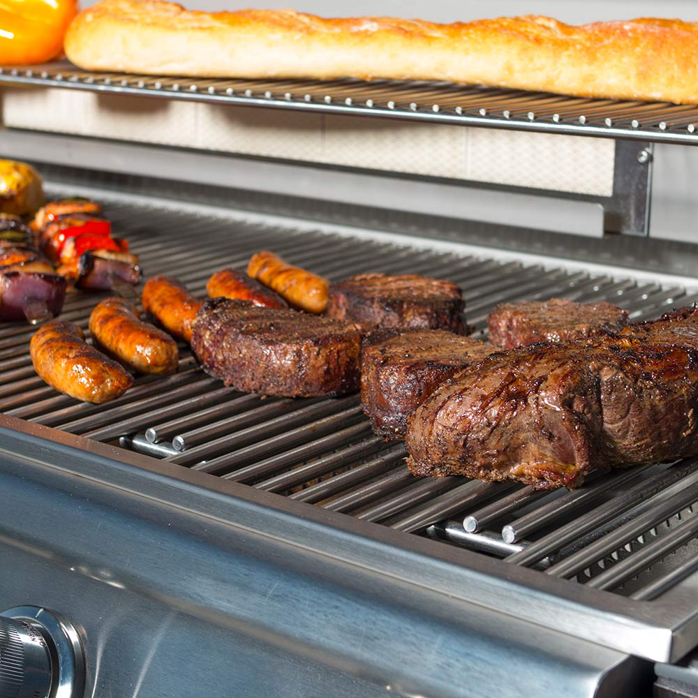Stainless Bull grill with food on cast grates: sausages and steaks, lid open