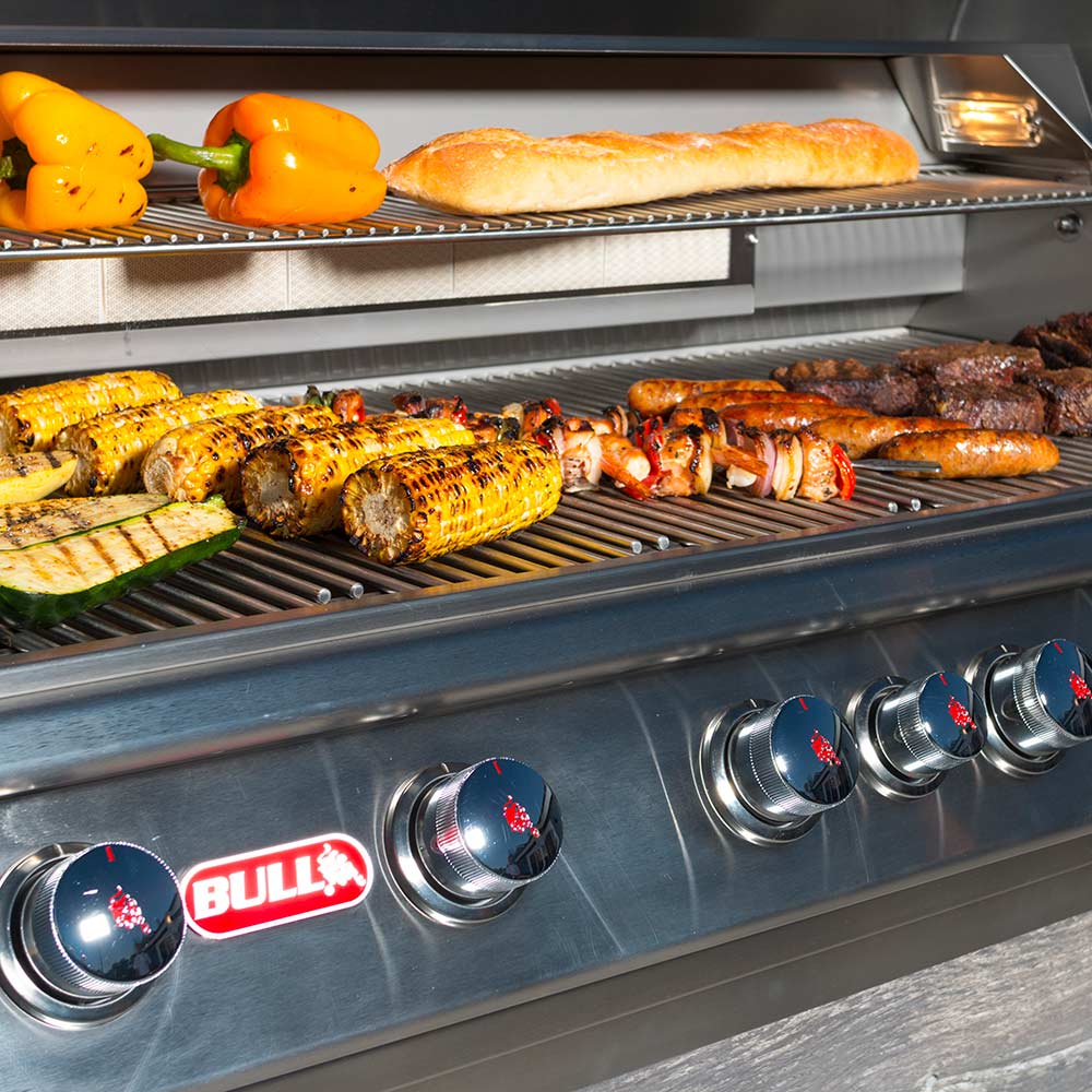 Stainless steel gas grill with BULL logo knobs and peppers and bread on grate