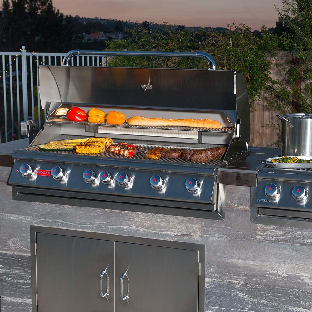 Stainless Bull grill with open hood, warming shelf, and cooking grates with food
