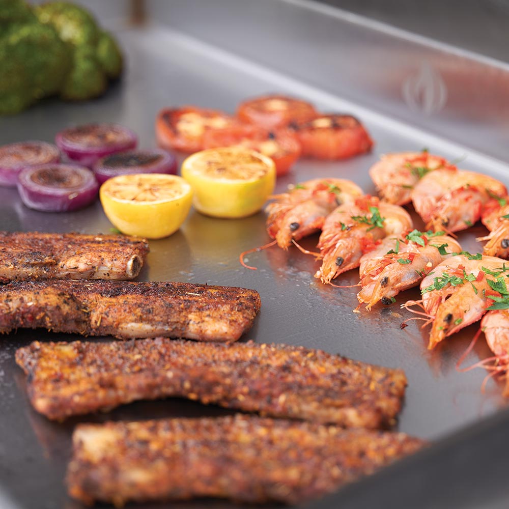 Close-up of food cooking on a flat top griddle surface, with smoke and juices
