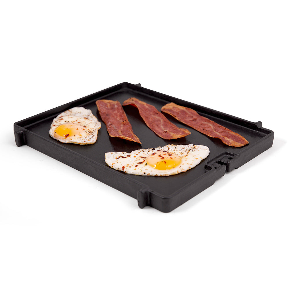 Cast iron side burner griddle with fried eggs and bacon strips, black surface