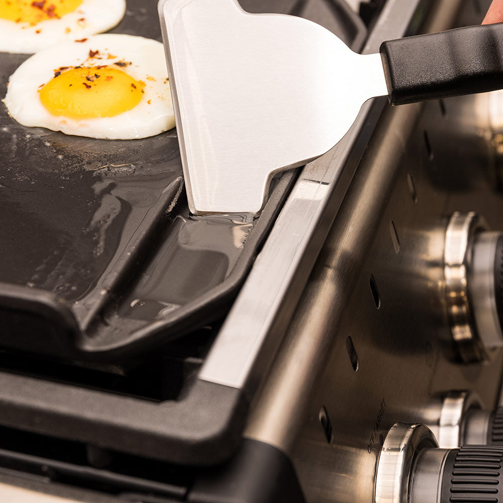 Cast iron griddle plancha with spatula lifting a fried egg