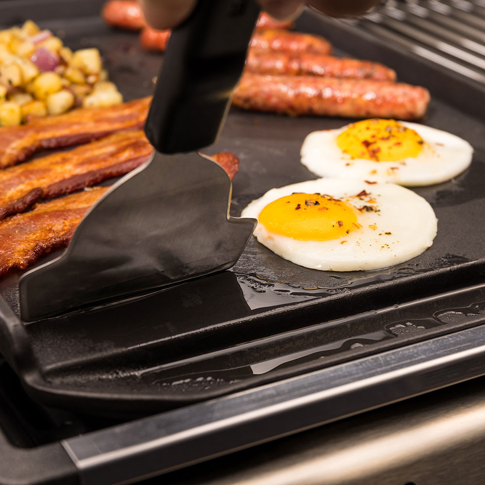 Cast iron griddle plancha with spatula serving food and two fried eggs