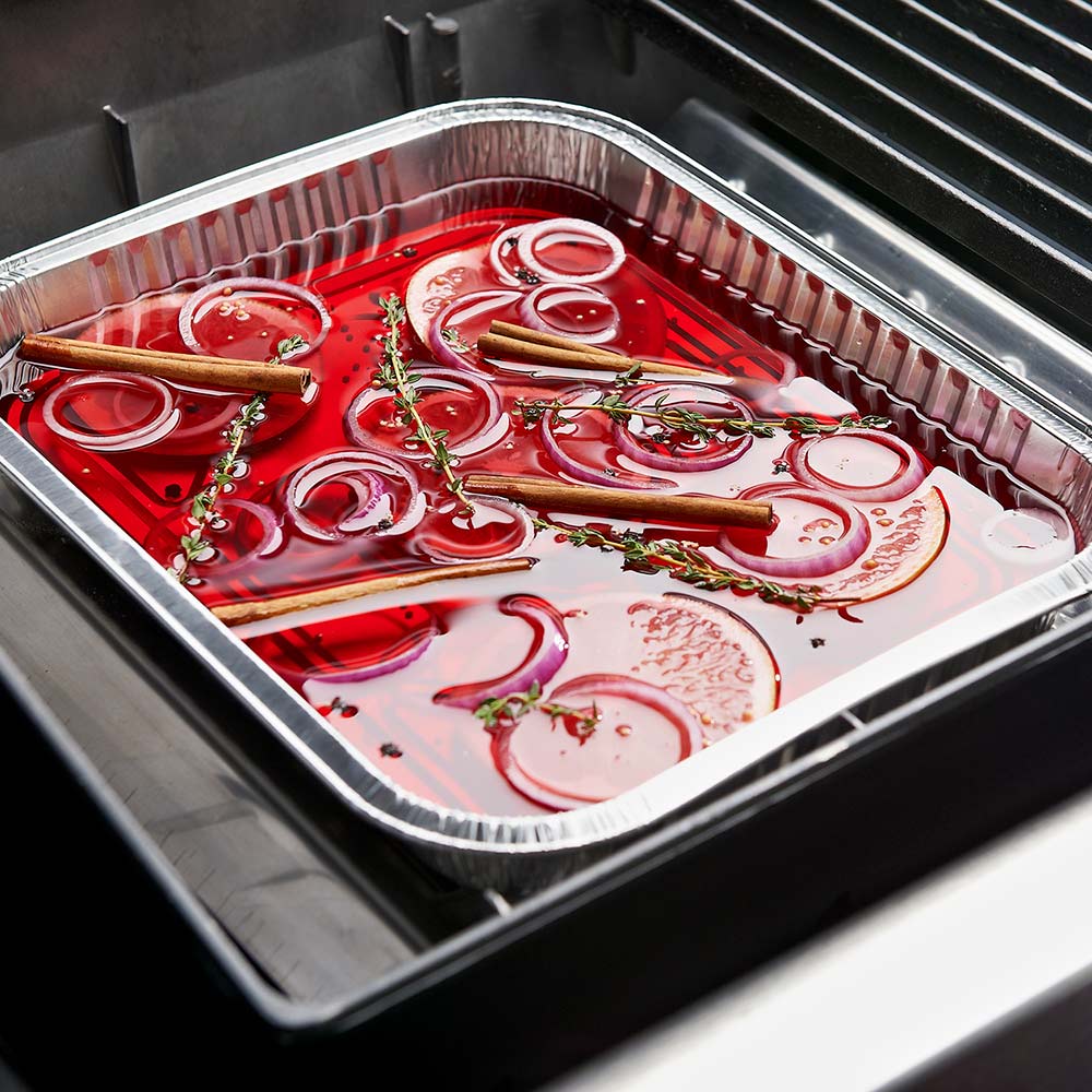Aluminum grill drip pan tray with red liquid, herbs, and onion rings