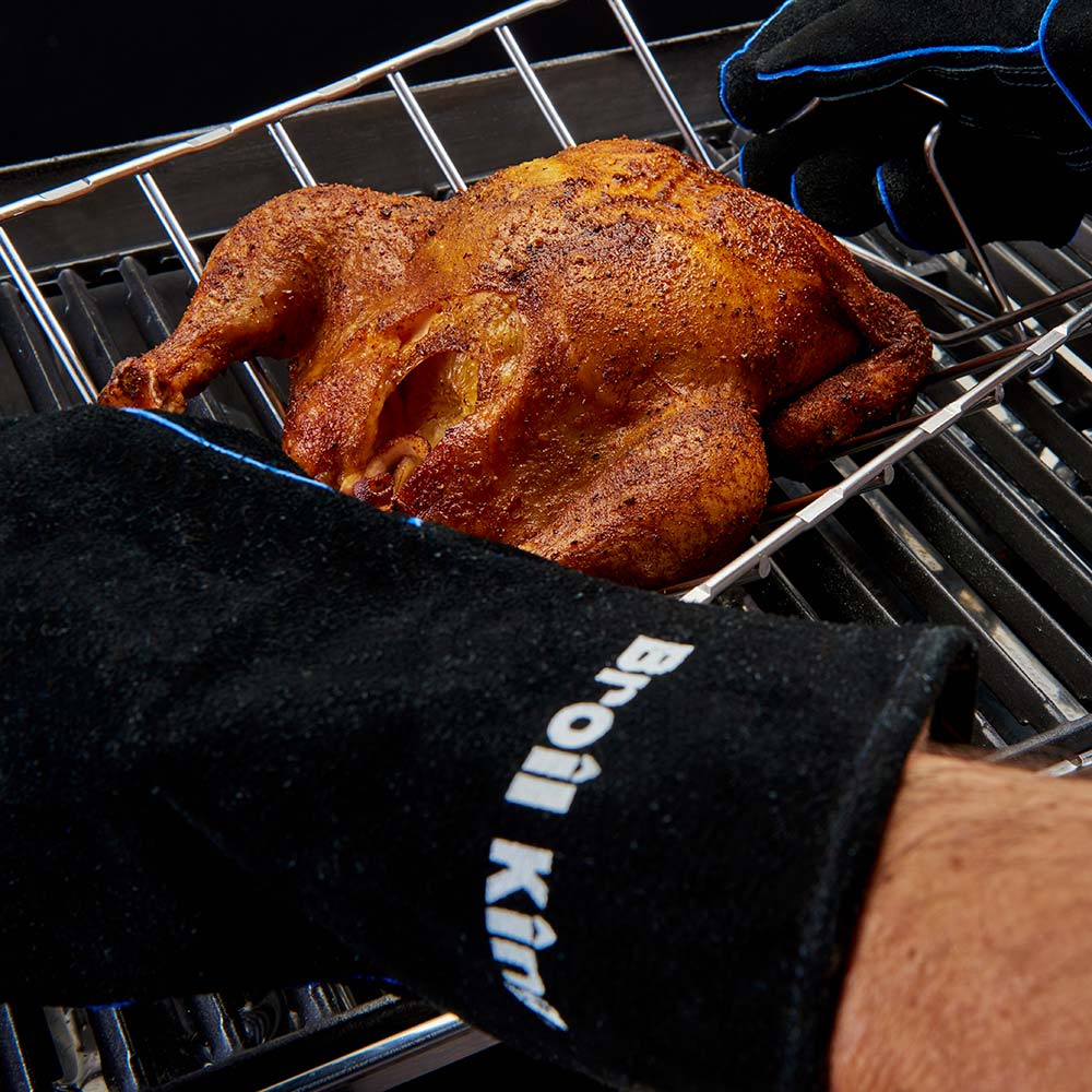 Black leather grill glove with blue trim holding cooked chicken on grill