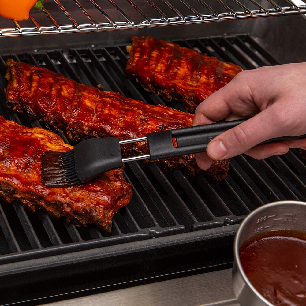 Grilling basting brush applying sauce on ribs on barbecue grill