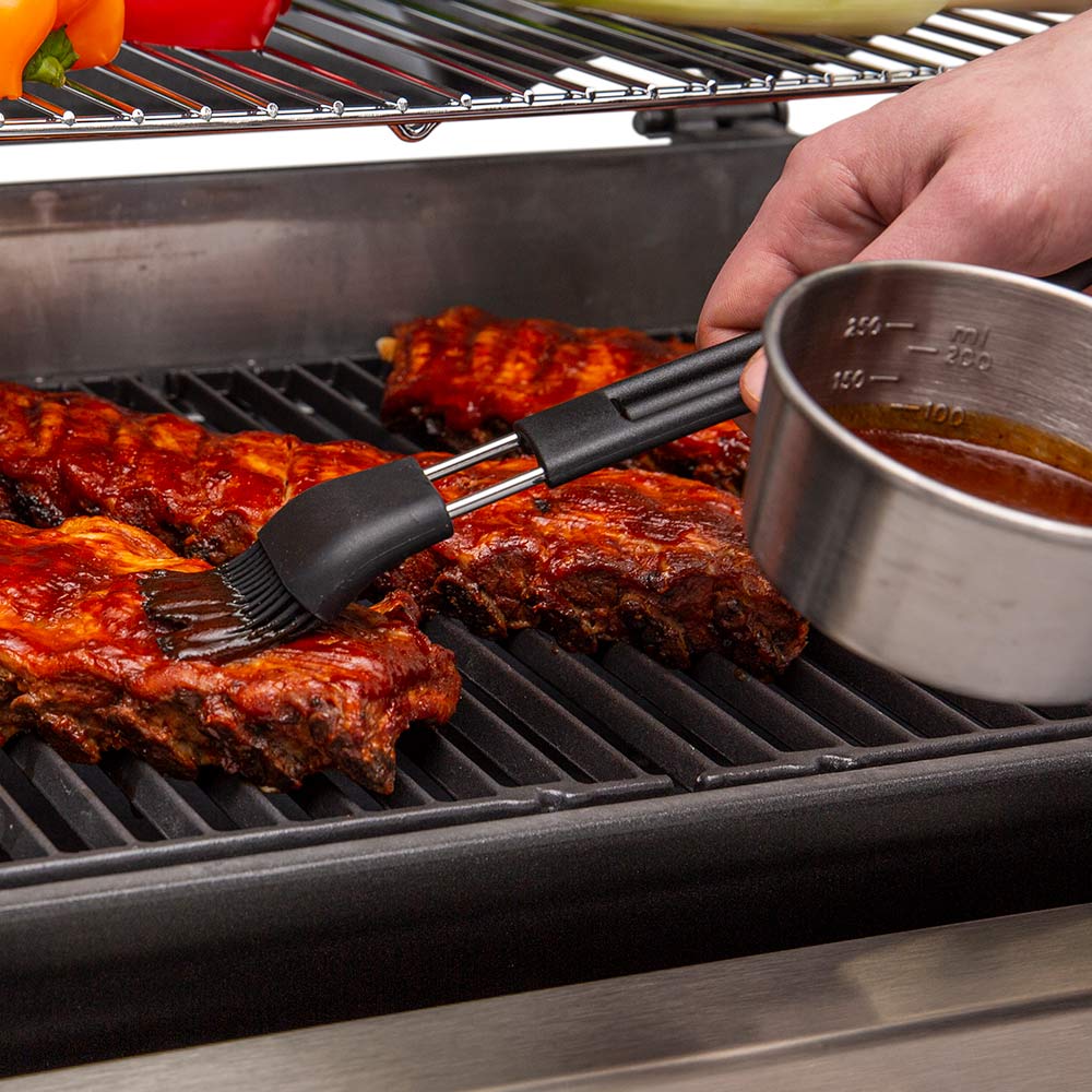 Basting brush in use on grilled meat with metal sauce cup