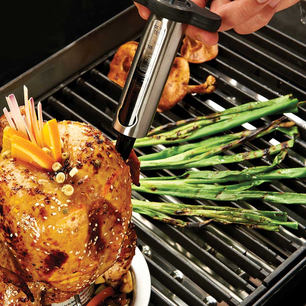 Marinade injector inserted into chicken on a grill with clear barrel and black handle