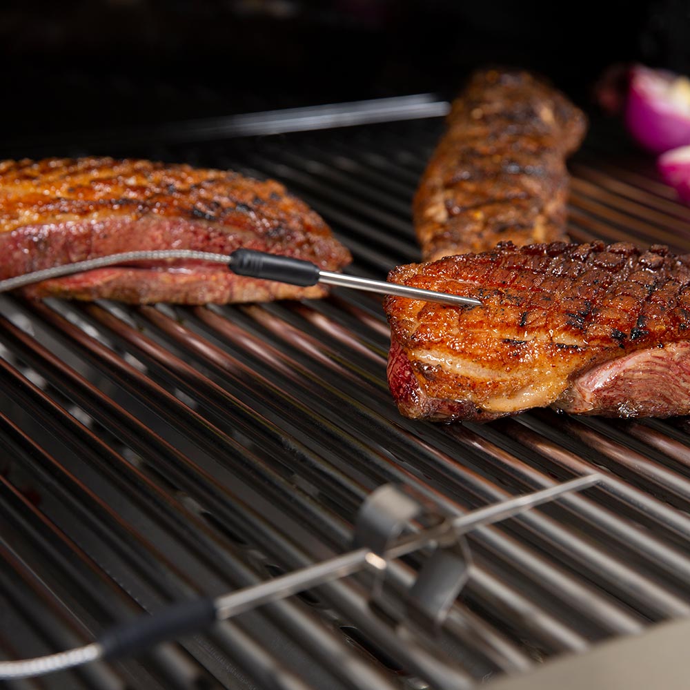 Stainless thermometer probe with black handle resting on grilled steak