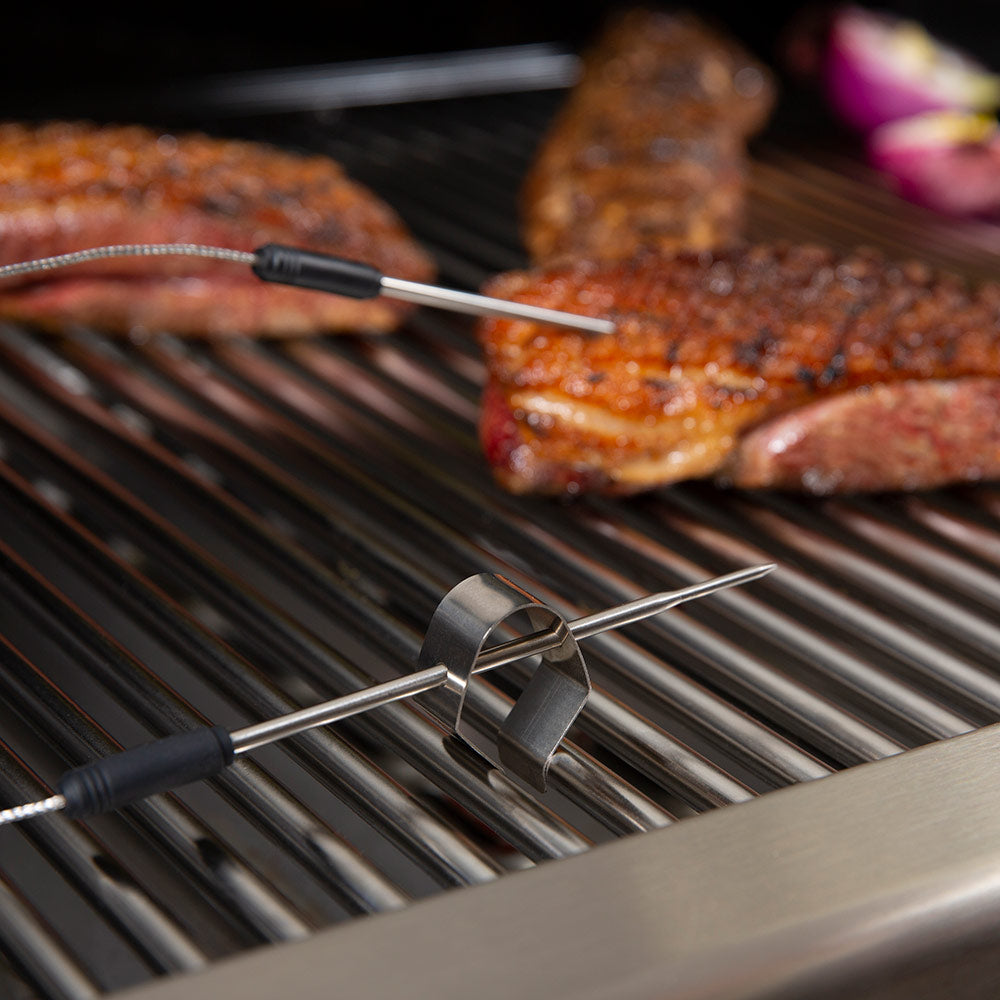 Stainless meat thermometer probes on grill near grilled steaks