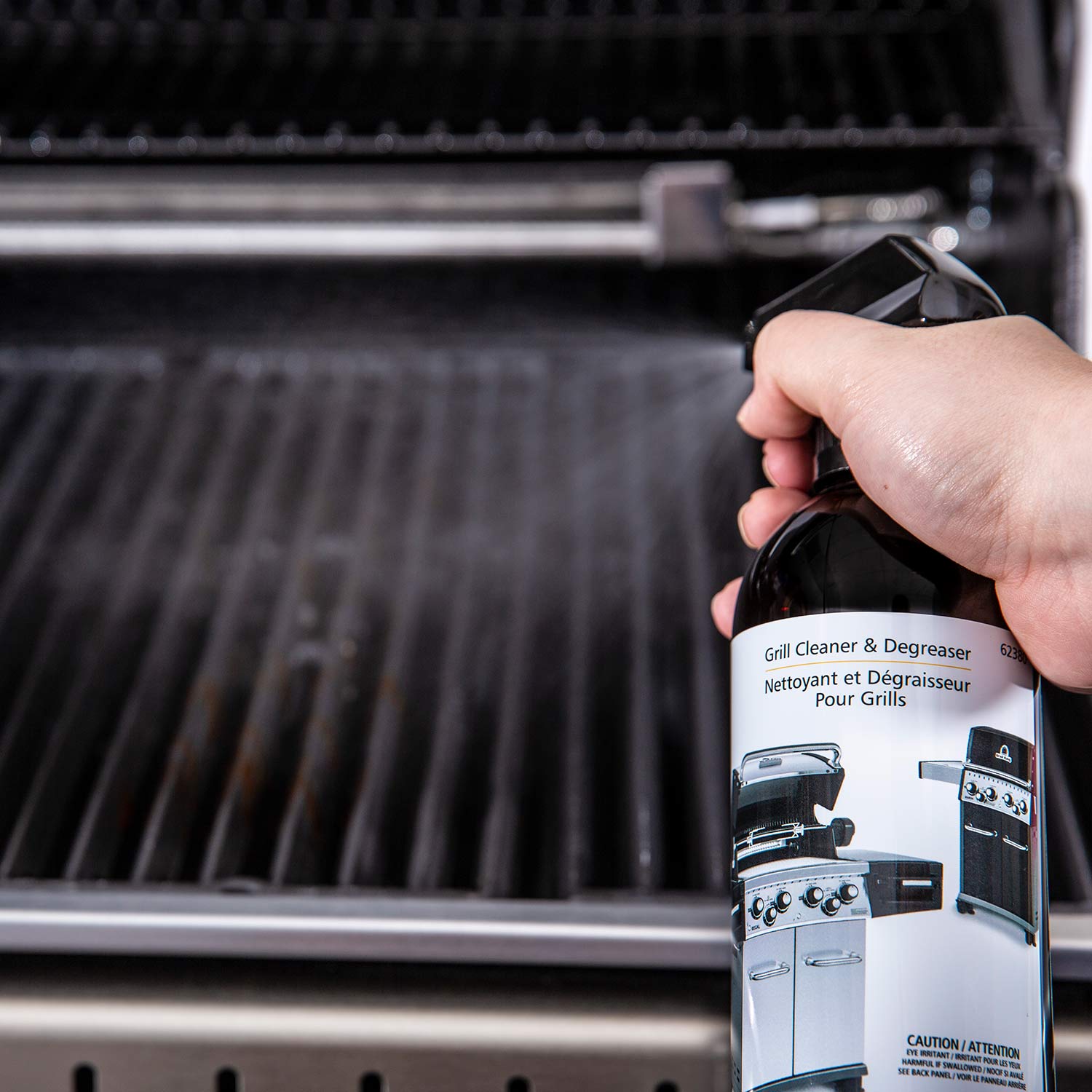 Hand holding a grill cleaner and degreaser bottle spraying the grill