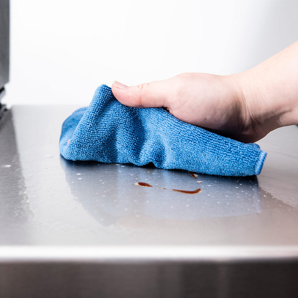 Blue microfiber cloth wiping a metal grill surface