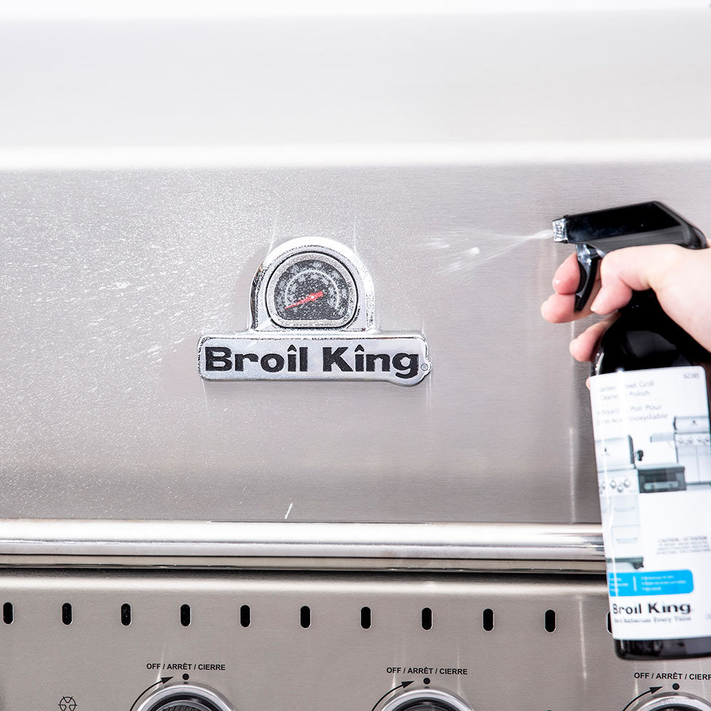 Hand spraying cleaner onto a stainless grill near the Broil King control panel
