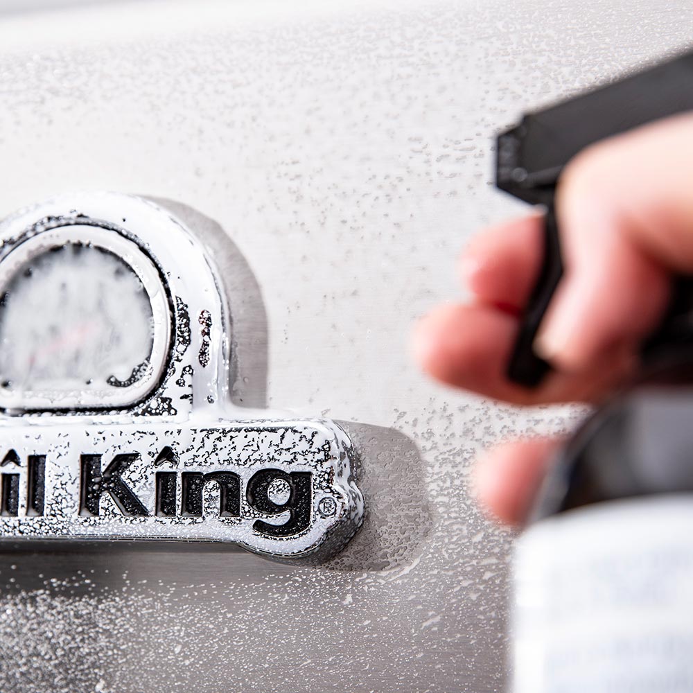 Close-up of cleaner spray on a stainless grill surface near the Broil King emblem