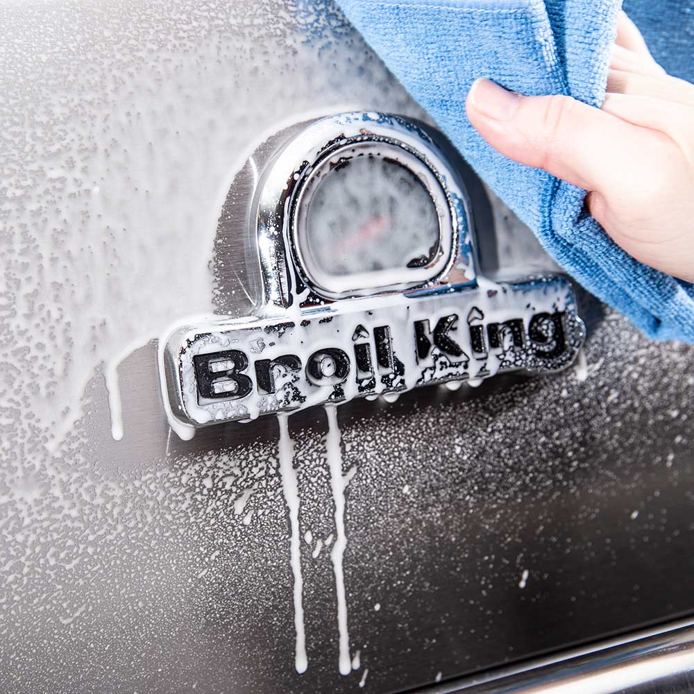 Blue cloth wiping cleaner from stainless grill around the Broil King logo