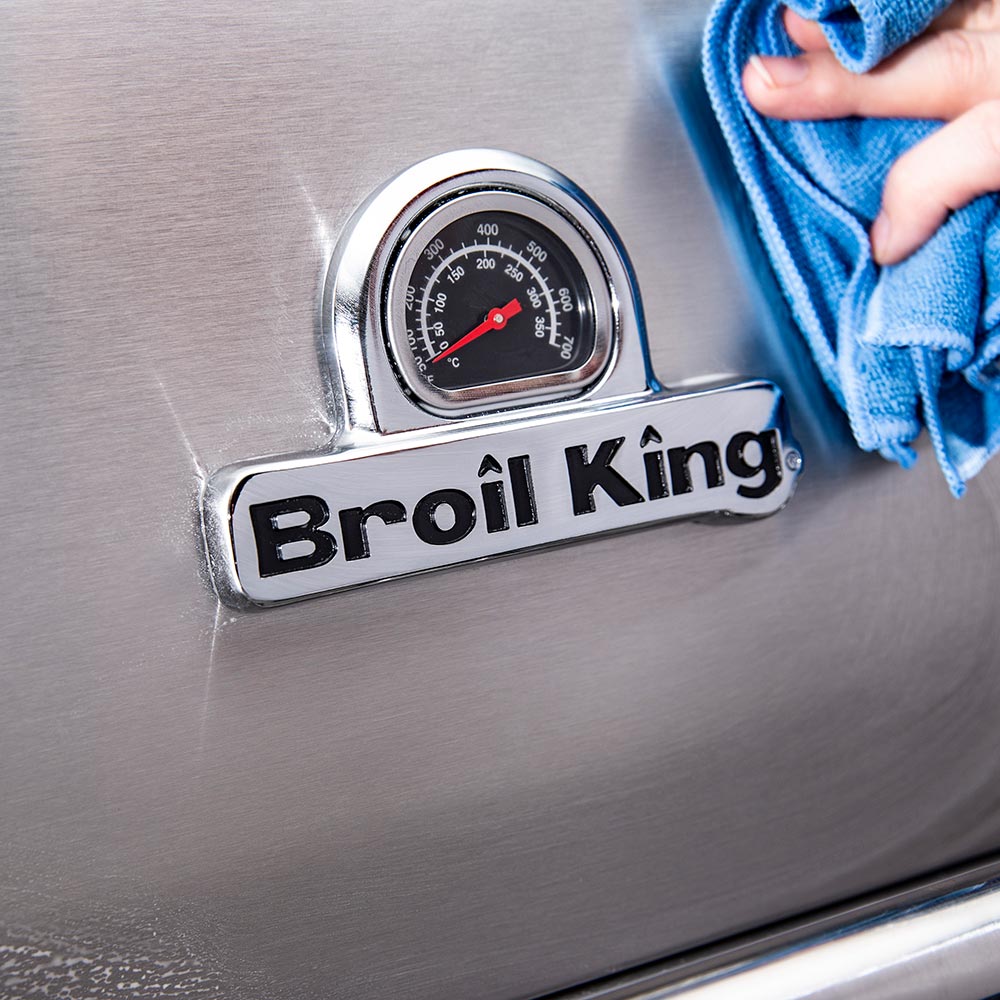 Stainless grill thermostat gauge being wiped with a blue cloth after cleaning