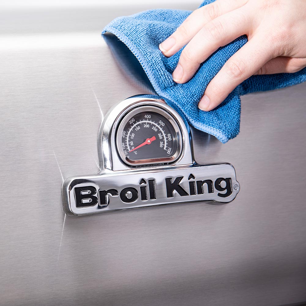 Broil King grill revitalizer cream on stainless grill, wiped with blue cloth over logo