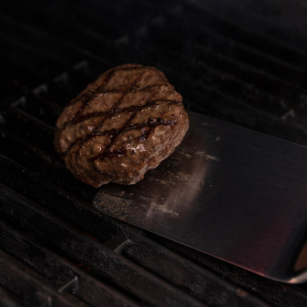 Grilled beef patty with browned grill marks on dark grill grate