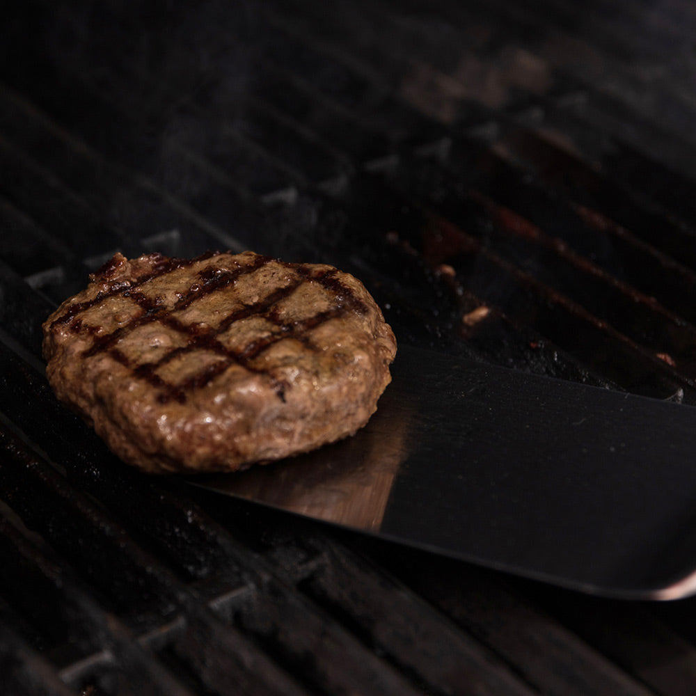 Grilled beef patty with crosshatch marks on dark grill grate