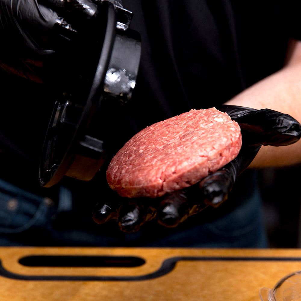 Gloved hands placing raw burger patty into burger press ring