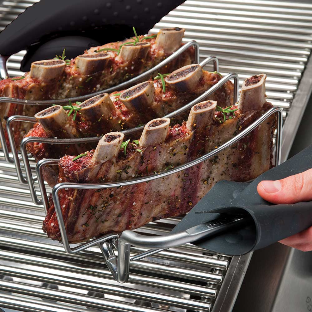 Stainless rib and roast rack with seasoned ribs on grill grates, held with tongs