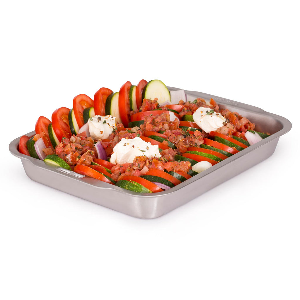 Stainless steel roasting and drip pan filled with sliced vegetables and herbs