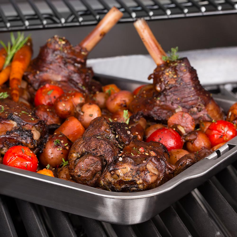 Stainless steel roasting and drip pan on grill with ribs and mixed vegetables