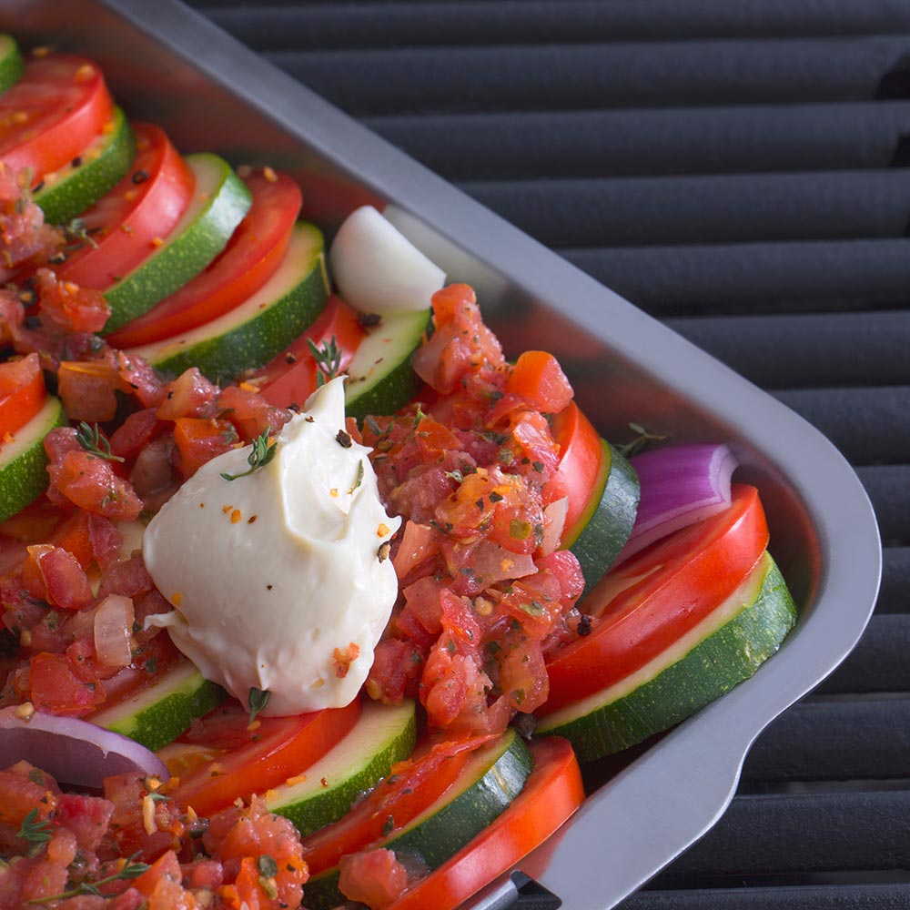 Stainless steel roasting and drip pan with sliced peppers, zucchini, and mozzarella