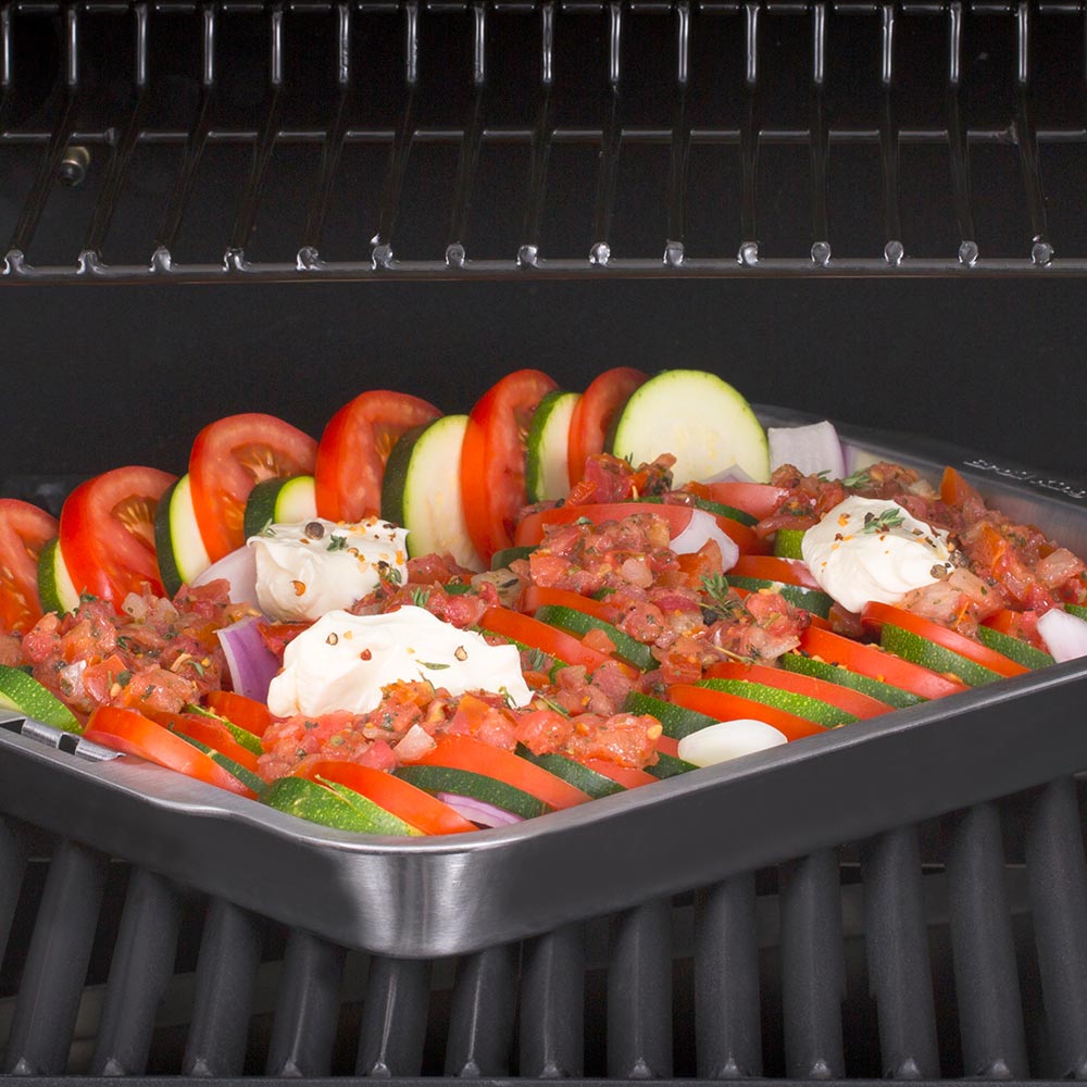 Stainless steel roasting and drip pan on grill with sliced vegetables and mozzarella