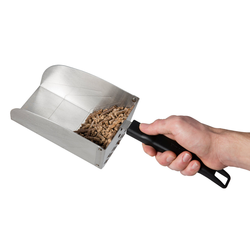 Metal scoop held in hand, filled with dark pellets or charcoal, black grip handle