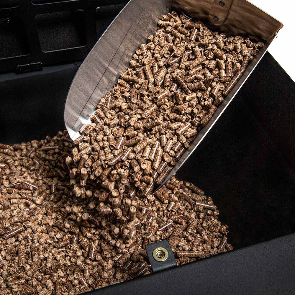 Pellets or charcoal spilling from metal scoop into a grill firebox