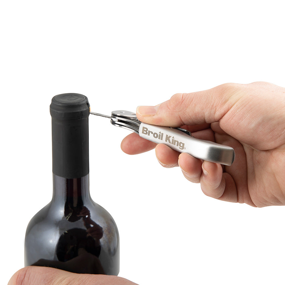 Wine bottle opener held in hand, chrome lever with corkscrew removing cork from bottle.
