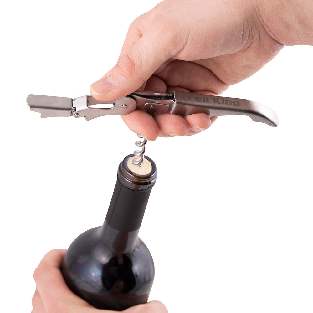 Wine bottle opener in hand, chrome lever positioned to pull the cork from a bottle.