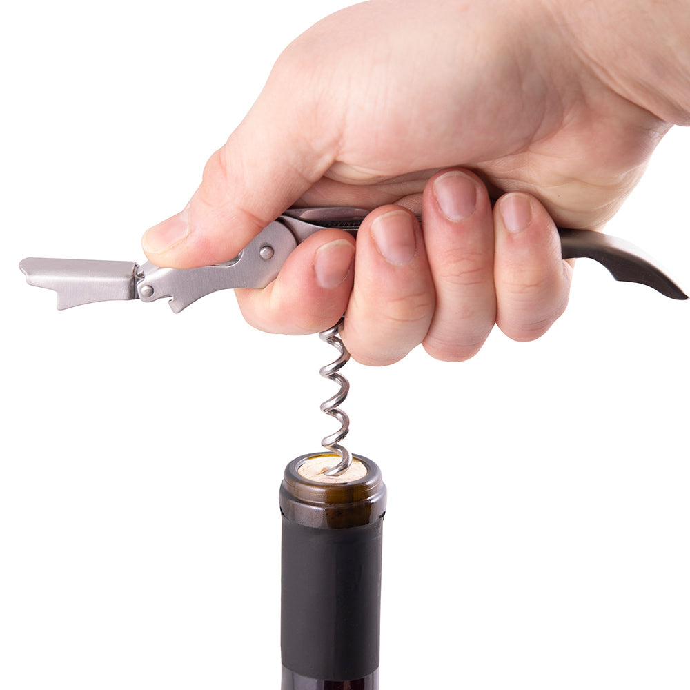 Wine bottle opener engaged on cork, chrome lever pulling from dark wine bottle.