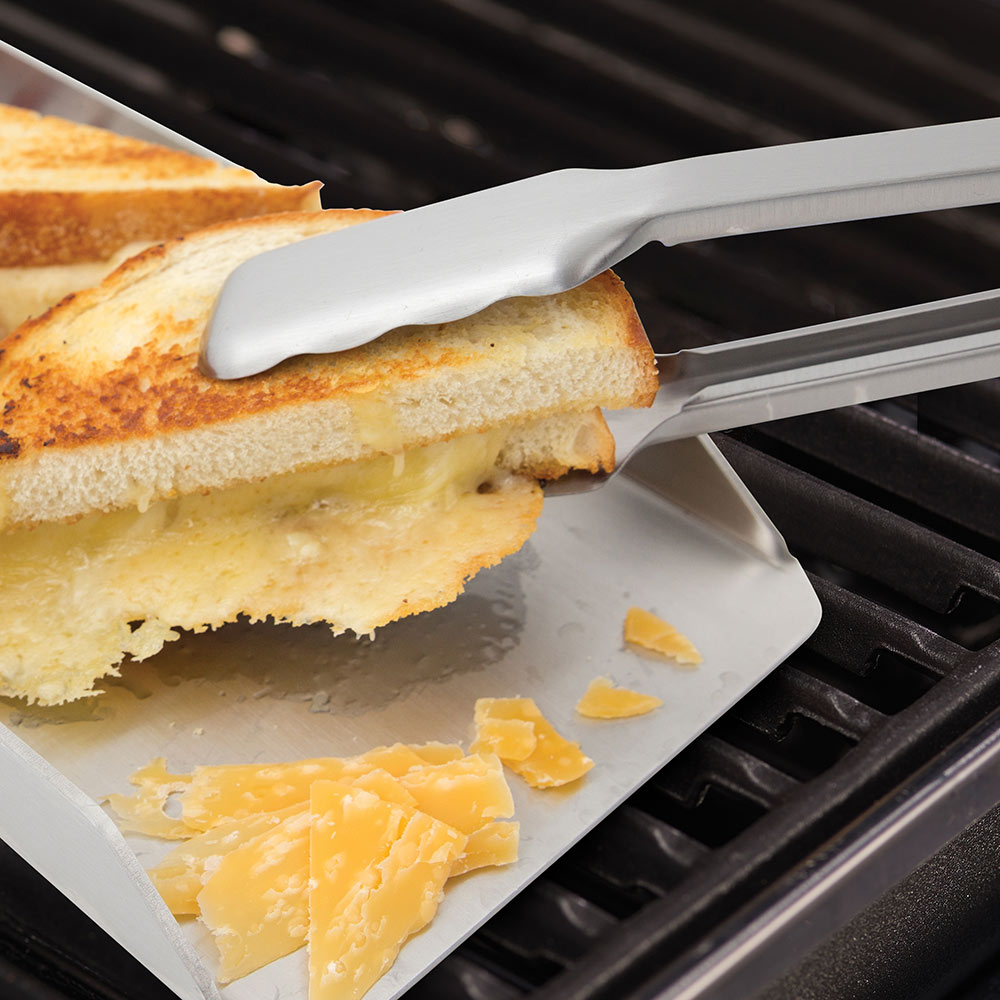 Grill tongs lifting grilled sandwich from grates