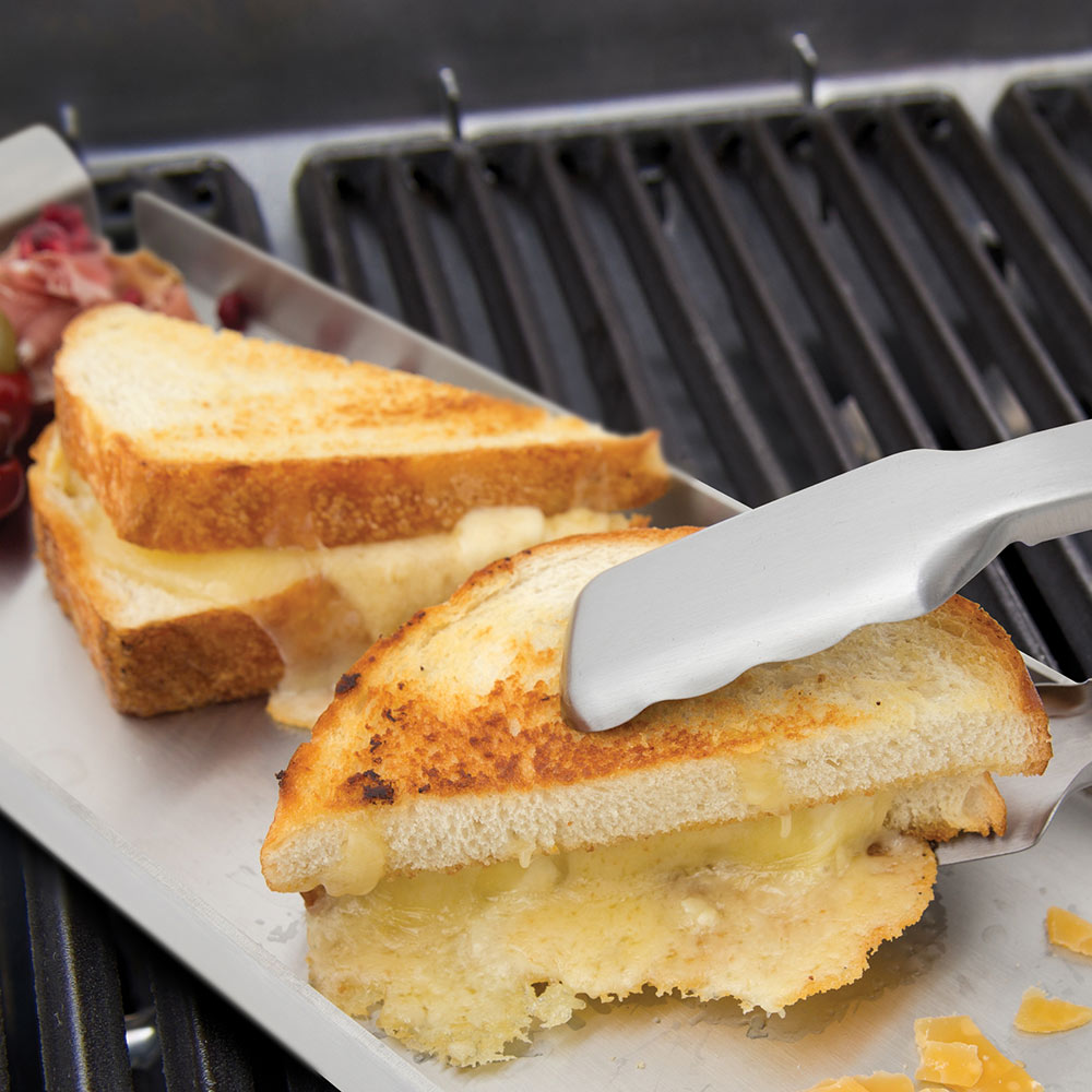 Grill tongs holding toasted bread on a tray over grill grates