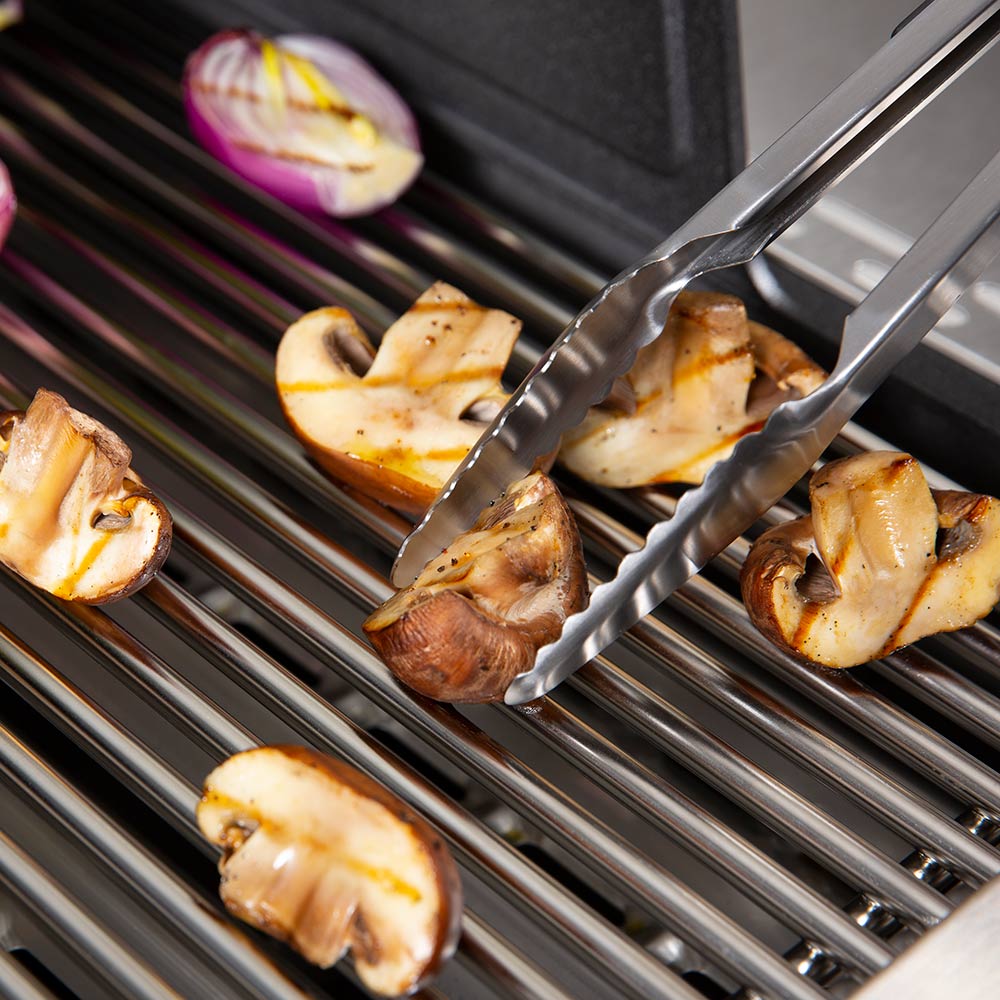 Broil King grill tongs holding charred sliced vegetables over the grate