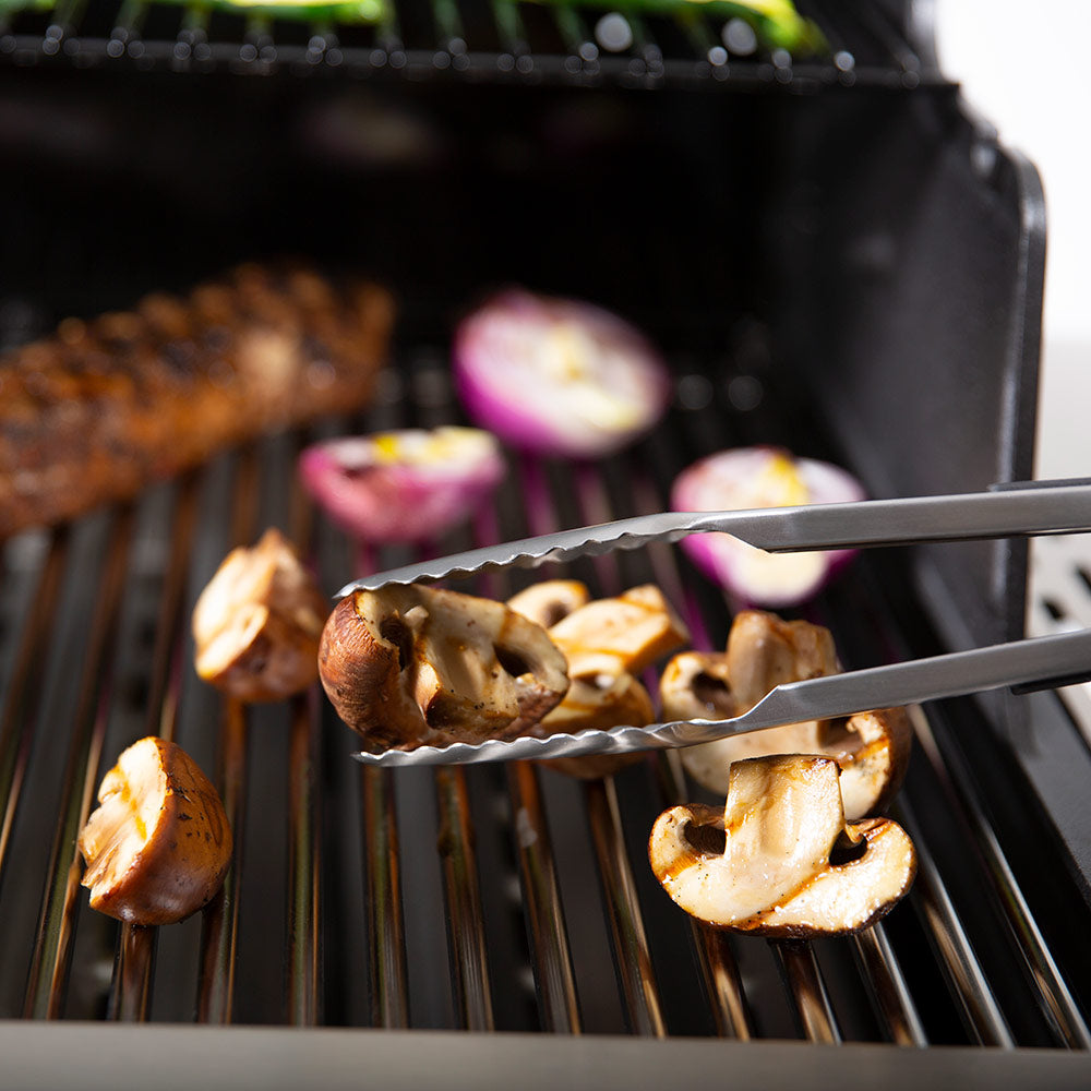 Broil King baron grill tongs gripping sliced vegetables on a hot grill