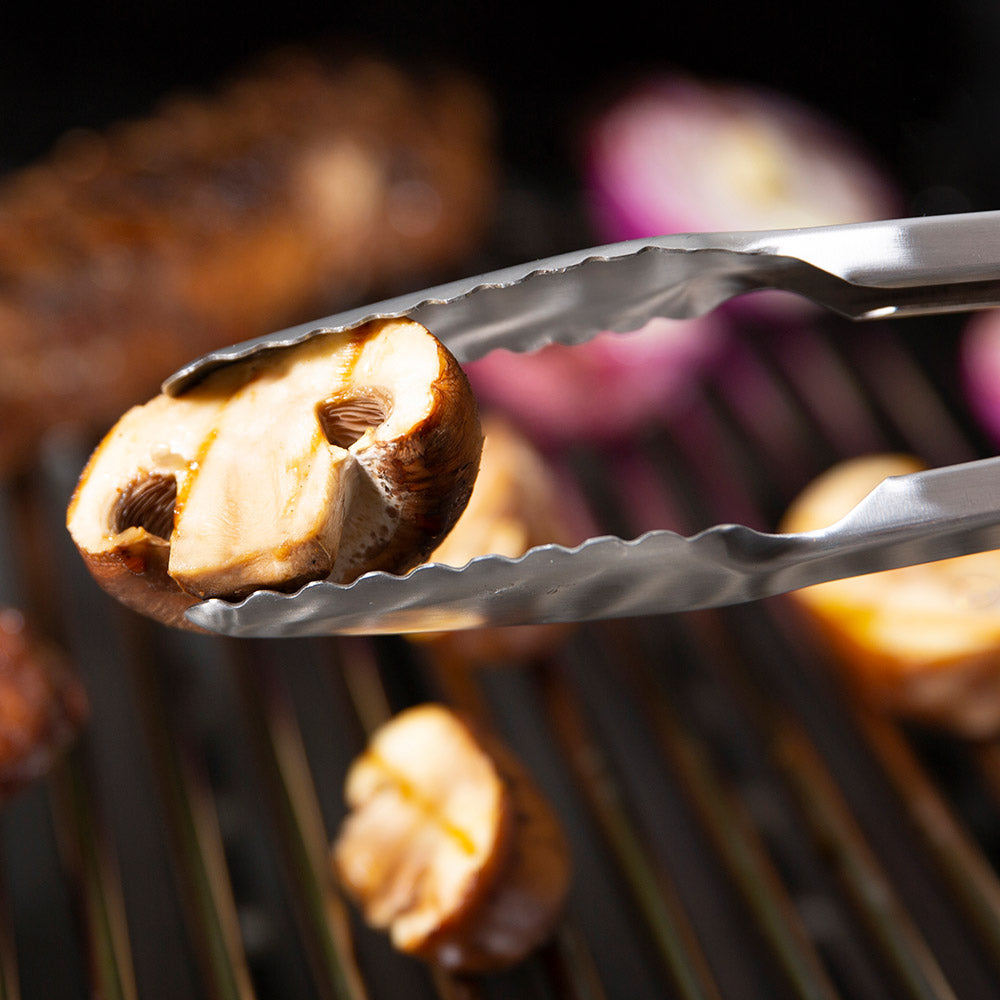 Barbecue tongs holding a grilled onion piece, serrated tips visible